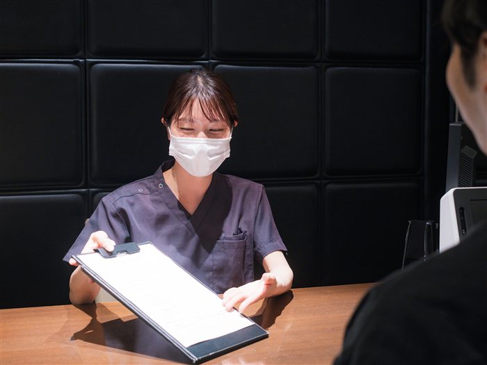 受付でスタッフが問診票を確認しながら説明する様子